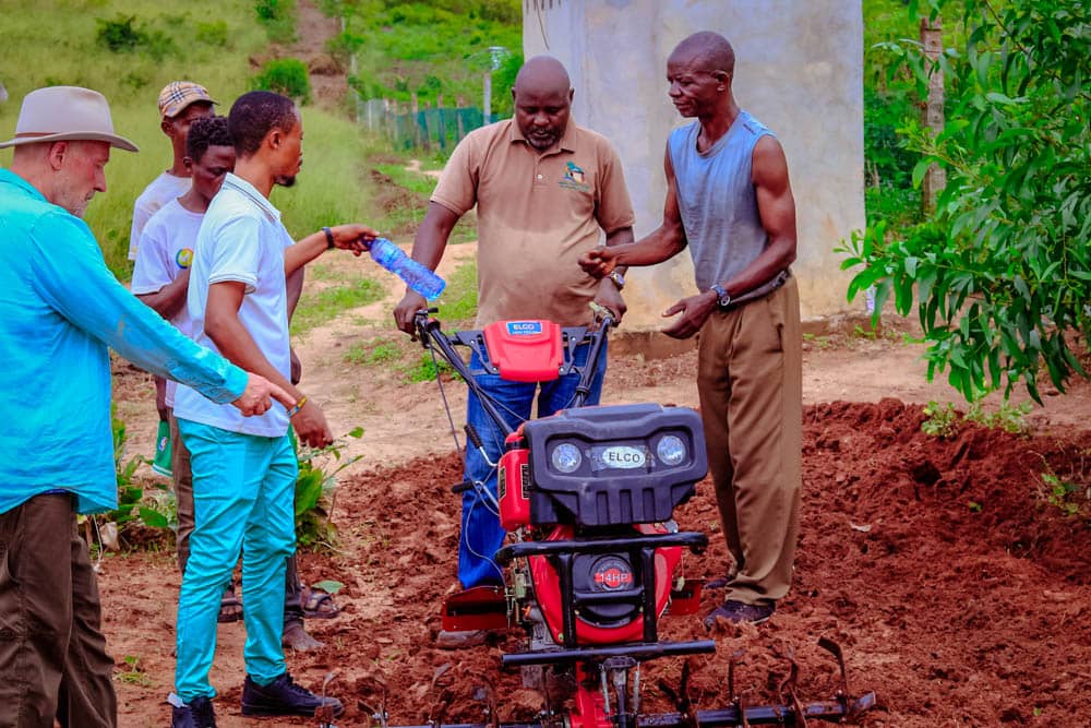 Farm partners demonstrating a power tiller on prepared soil